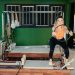 Fitness enthusiast practicing Pilates on a reformer machine in a modern, brightly lit studio.